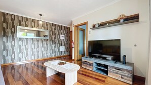 A modern living room with a wooden floor, a round coffee table, a flat-screen TV, and a built-in entertainment unit. - Judite Home Apartment by Atlantic Holiday (Santa Cruz)