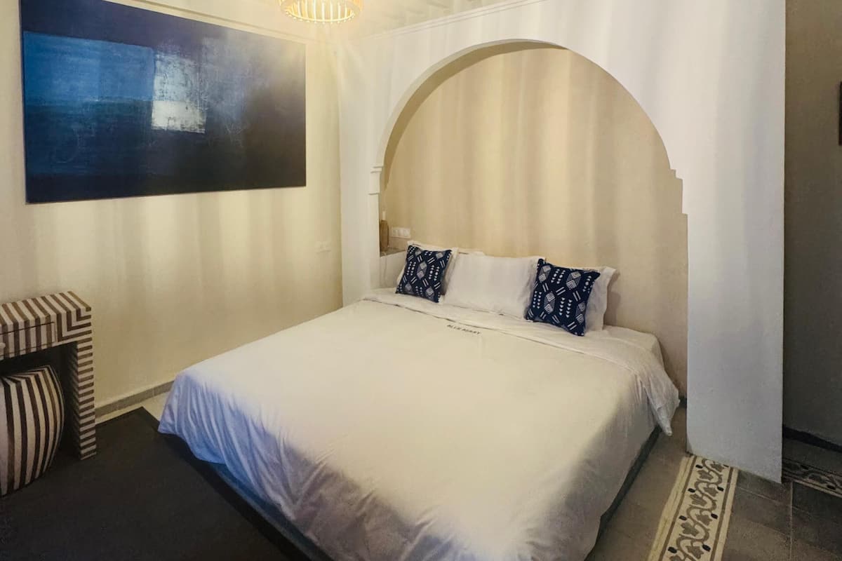 A bedroom with a large bed, a hanging light fixture, and a partial view of a bathroom.