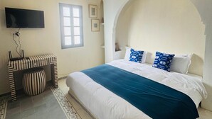 A bedroom with a large bed, a television, a decorative bench, and a patterned rug. - Riad Blue Berry (Marrakech)
