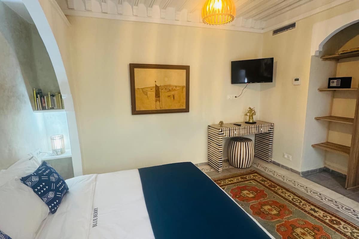 A bedroom with a bed, a television, a rug, and a painting on the wall.