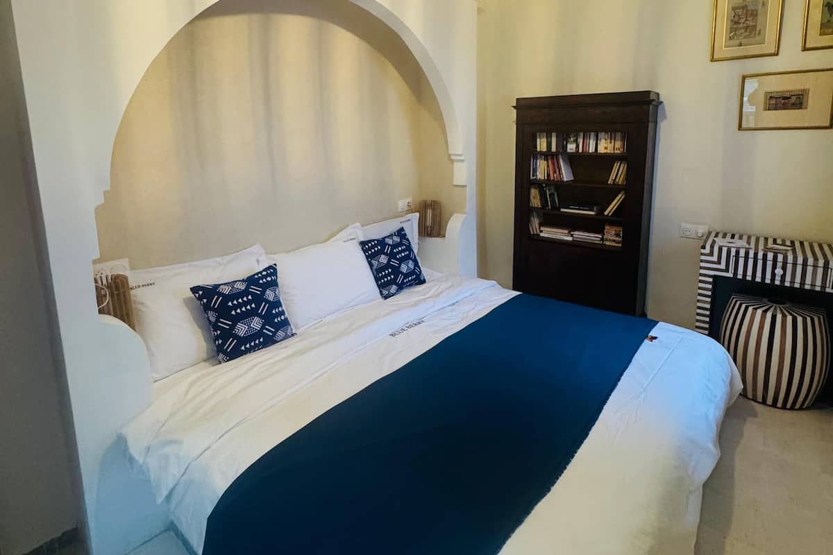 A hotel room with a large bed, a dark wooden wardrobe, and a ceiling with decorative molding.