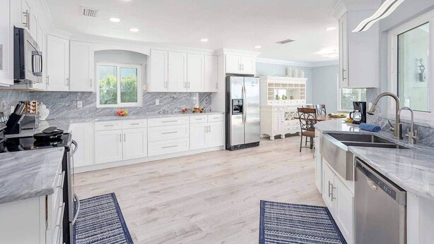 Una cocina moderna con armarios blancos, encimera de mármol y refrigerador de acero inoxidable.