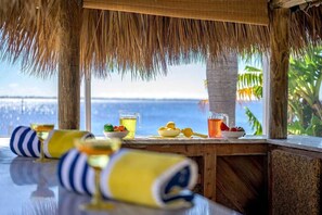 A wooden table with drinks and fruits, a straw hat, and a view of the sea. - TikiTime Tropical Riverfront Retreat (Cape Coral)