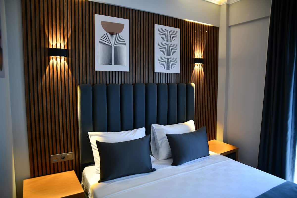 A modern hotel room with a large bed, dark headboard, and two bedside tables with lamps.