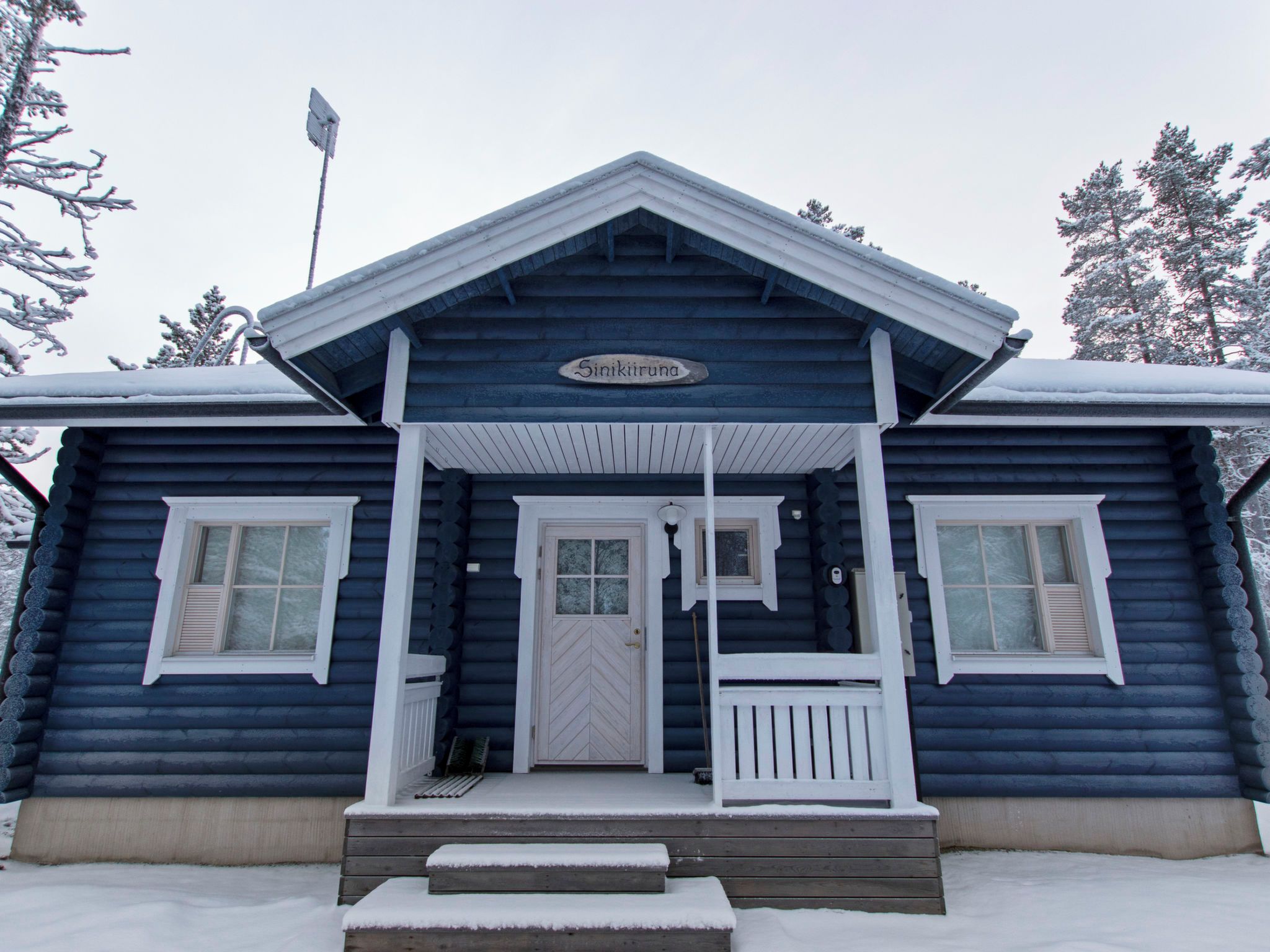 Een vakantiehuis van hout met een veranda, een witte deur en een bord met de tekst 'Sinikiruna'.
