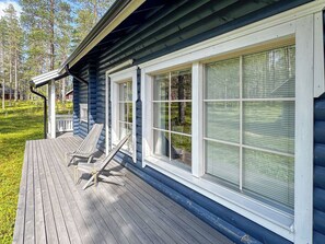 A wooden deck with two lounge chairs, a house with large windows, and a forested background.