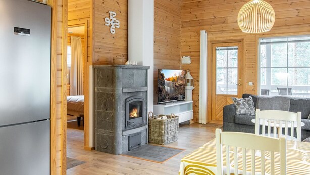 A cozy log cabin interior with a stone fireplace, wooden walls, a modern kitchen, and a comfortable seating area.