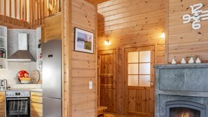A cozy log cabin interior with a kitchen, a fireplace, and a wooden door with frosted glass panels.