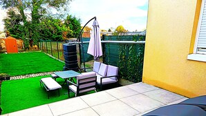A patio with a tiled floor, a table, two chairs, and a small garden area with a lawn and a fence. - Le Logis du Jardin Anzin (Anzin)