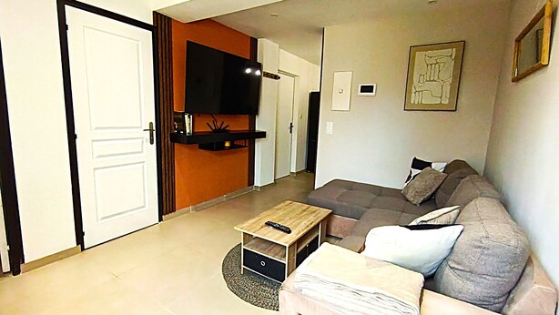A living room with a sofa, a coffee table, and a TV mounted on the wall. - Le Logis du Jardin Anzin (Anzin)