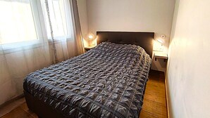 A bedroom with a bed, two bedside tables, and a window with curtains. - Le Logis du Jardin Anzin (Anzin)