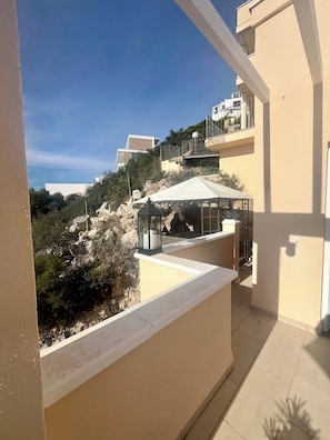 A balcony with a view of a hillside, a pergola, and a building in the background. - Duplex with swimming pool, jacuzzi, garage, with 180º panoramic sea view terraces (Peñíscola)