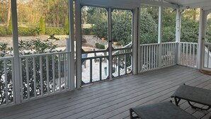 A covered outdoor area with a wooden deck, white railings, and a view of a landscaped garden. - Golf course home in Raintree Country Club. Outdoor oasis with pool and hot tub. (Charlotte)