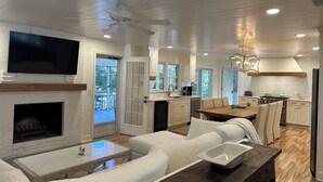 A modern living room with a fireplace, white sofas, a coffee table, and a TV mounted on the wall. - Golf course home in Raintree Country Club. Outdoor oasis with pool and hot tub. (Charlotte)