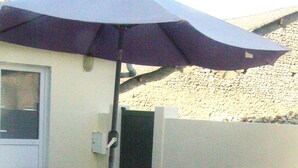 Una veranda esterna con tavolo in vetro e sedie in metallo bianco, riparata da un ombrellone grande.