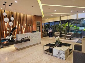 A modern hotel lobby with a reception desk labeled "TOWER 2", seating area, and large windows with plants. - Cozy and Comfy Retreat with Balcony (Parañaque)