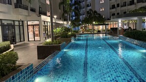 Una piscina con bordes de azulejos, rodeada de edificios con balcones y algunas palmeras.