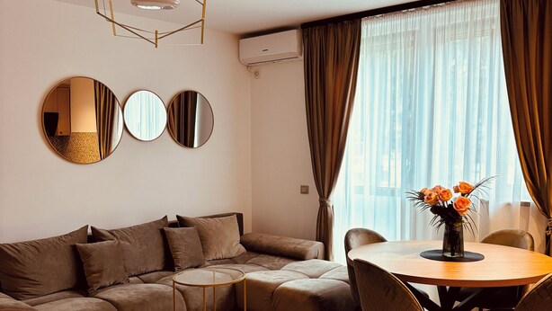 Una sala de estar moderna con un sofá seccional, una mesa de comedor redonda con sillas, una mesita auxiliar y un jarrón con flores.