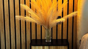 A bedside table with a vase of dried pampas grass and a lamp.