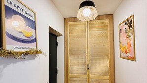 Un pasillo con suelo de madera, una lámpara colgante negra, una puerta de madera con listones horizontales y dos cuadros enmarcados en las paredes.