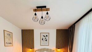 Un dormitorio con una cama grande, dos mesitas de noche, un cabecero de madera, una lámpara colgante y dos cuadros en la pared.