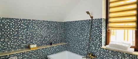 Un baño con una bañera independiente, una ventana con persianas y un salpicadero de azulejos.
