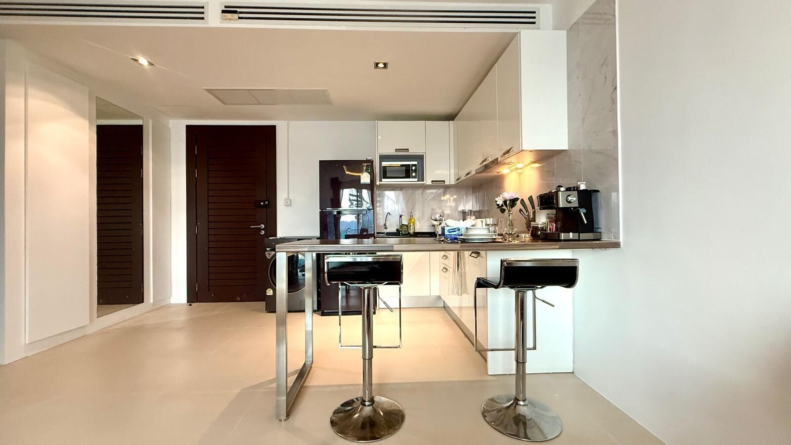 A modern kitchen with a central island, bar stools, a microwave, and a sink.