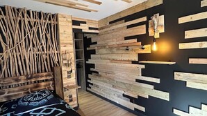 Une chambre moderne avec un plafond en bois, un lit recouvert d’une couvre-lit à motifs noir et blanc, et un luminaire fixé au mur.