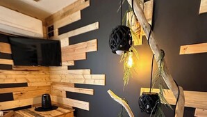 Une chambre moderne avec un banc en bois, un téléviseur fixé au mur et un luminaire original en forme d’arbre.
