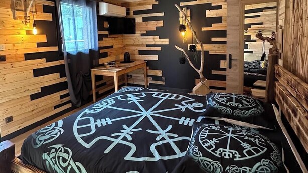 Une chambre confortable avec un plafond en bois, un lit recouvert d’une courtepointe à motifs, une petite table et une chaise.