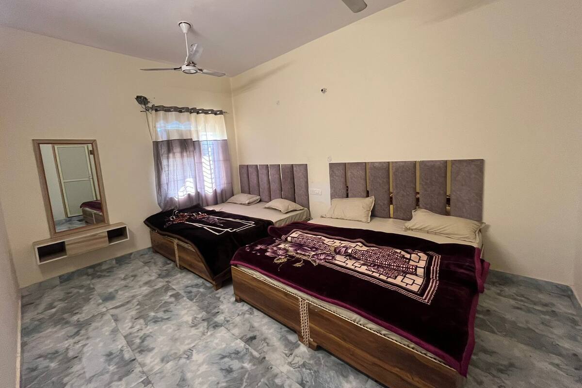 A bedroom with two beds, a ceiling fan, a window with curtains, and a mirror.