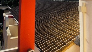 Vue d’un toit recouvert de tuiles, prise depuis un balcon, avec une colonne rouge au premier plan.