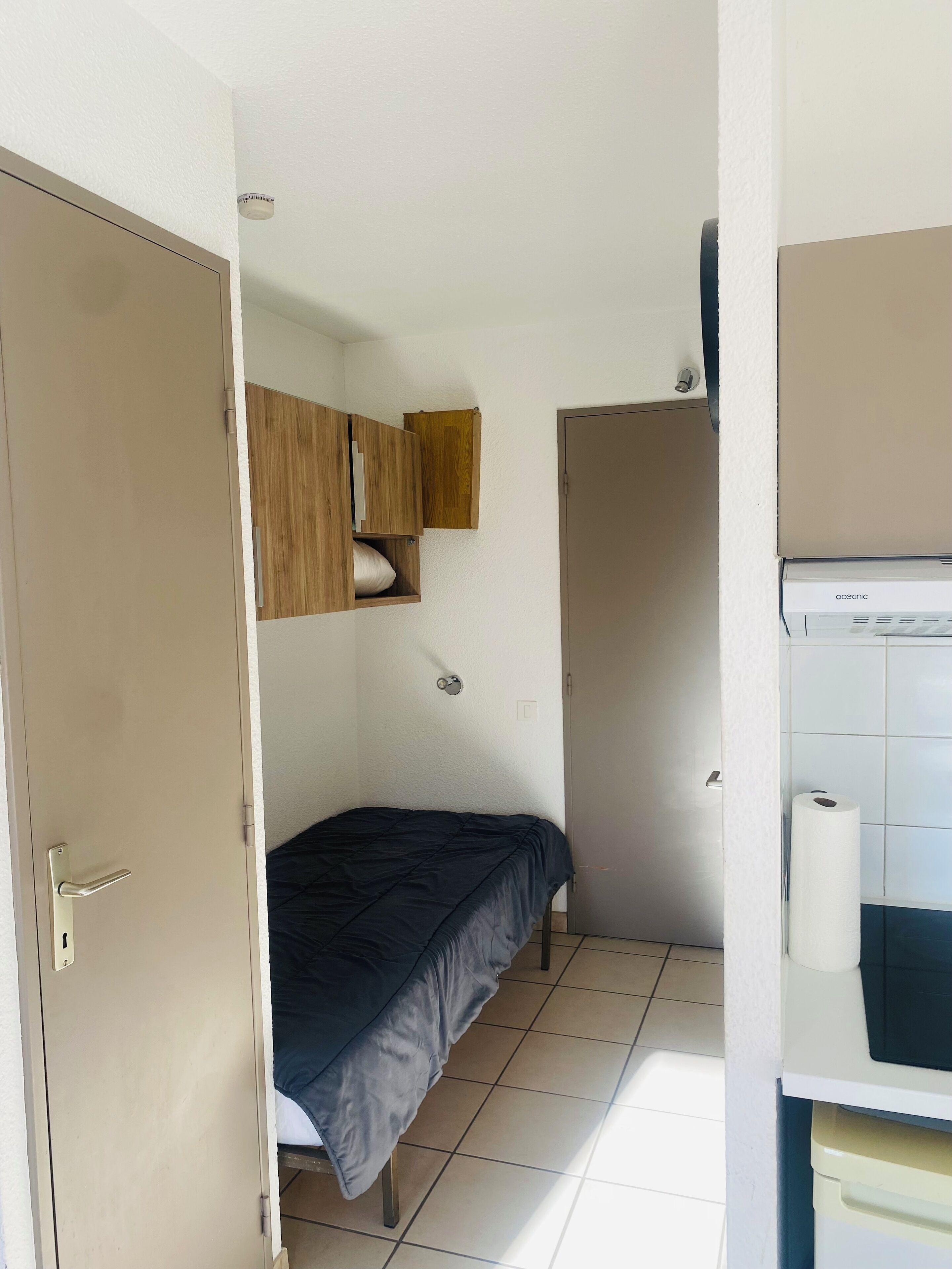 Quarto compacto com cama, guarda-roupa, pequeno armário e sanita.