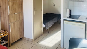 Une petite chambre comprenant un lit, un coin cuisine et une armoire.