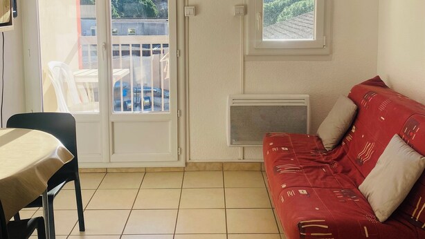 Une pièce avec un canapé rouge, une table à manger, une chaise, une porte-fenêtre coulissante, une fenêtre et un ventilateur de plafond.