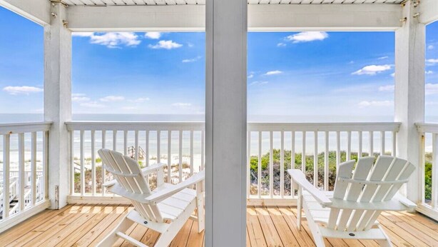 Una terraza de madera con dos sillas Adirondack blancas mirando hacia la playa.