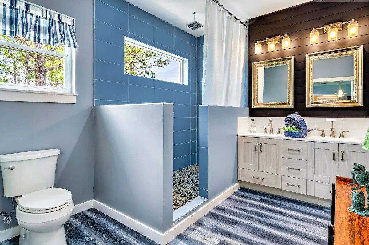 A modern bathroom with a blue accent wall, a shower with a pebble floor, a white toilet, and a vanity with a mirror and lights.