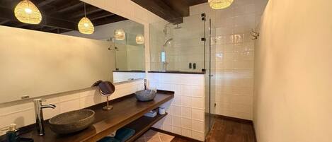 Une salle de bain moderne avec un grand miroir, un meuble-lavabo en bois, une cabine de douche en verre et des luminaires suspendus.