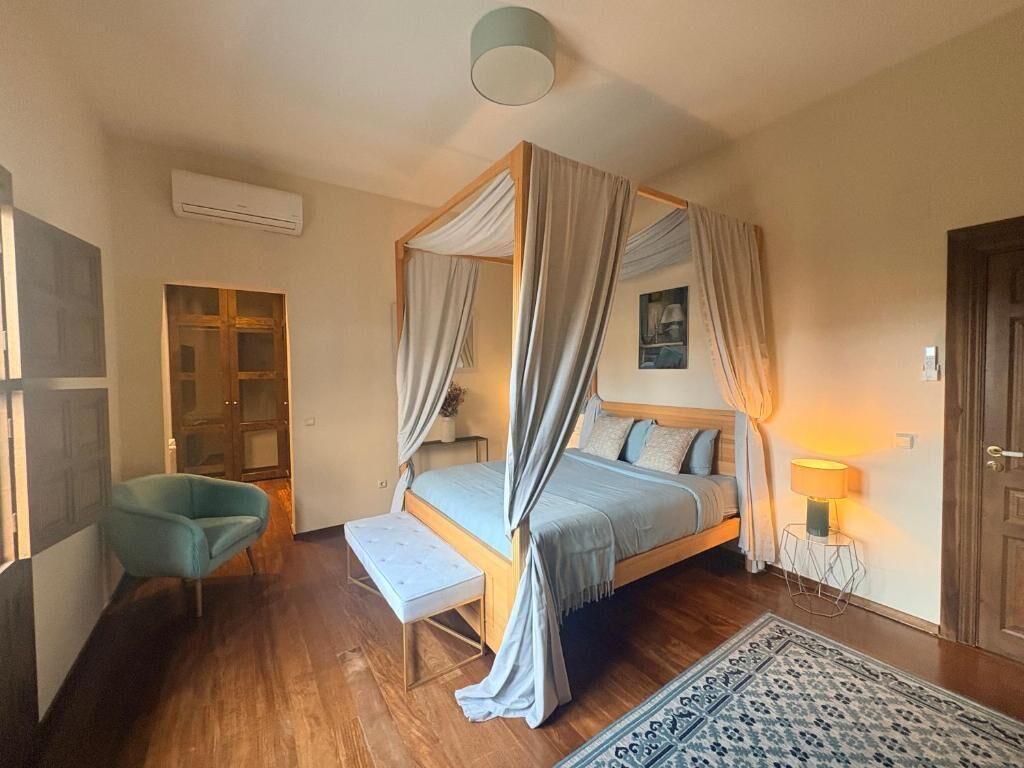 A bedroom with a four-poster bed, a bench, a small table with a lamp, and a patterned rug.