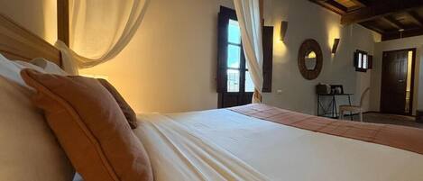 A bedroom with a bed, a window, a mirror, and a small table with a chair.