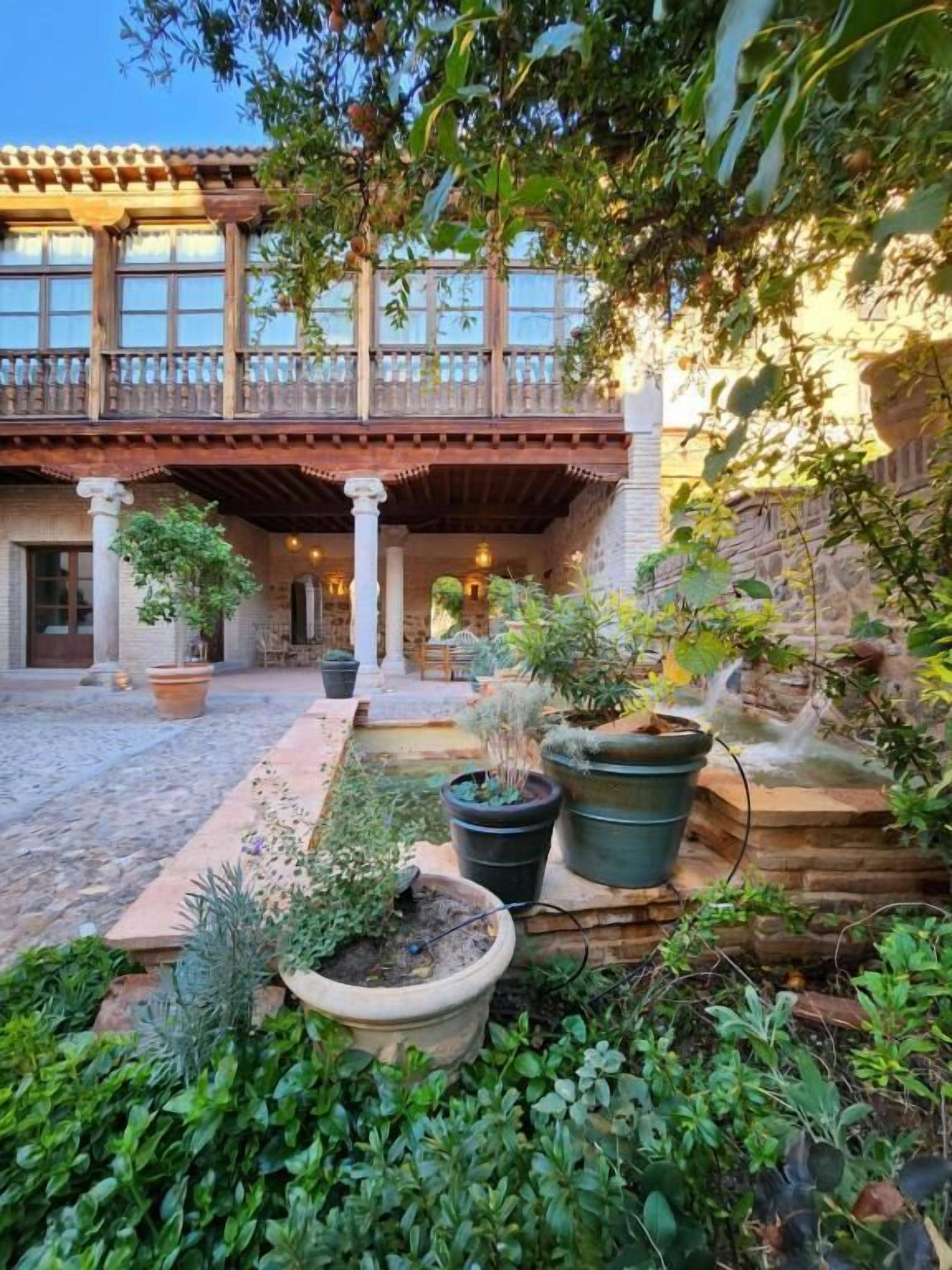 A courtyard with a covered patio, potted plants, and a stone wall.