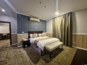 Ein Hotelzimmer mit einem großen Bett, einem Nachttisch, einer Klimaanlage, einem Schreibtisch mit Stuhl und einem fenster mit Vorhängen.