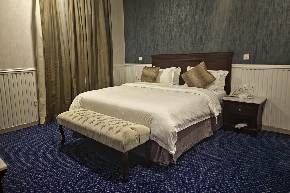 Ein Hotelzimmer mit einem großen Bett, einem Nachttisch mit Telefon und einer Bank.