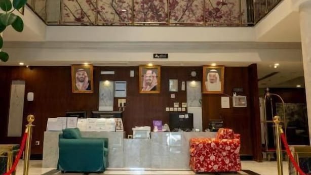En hotellobby med ett marmorgolv, en receptionsdisk, en kristallkrona och en balkong prydd med en väggmålning med blommotiv.