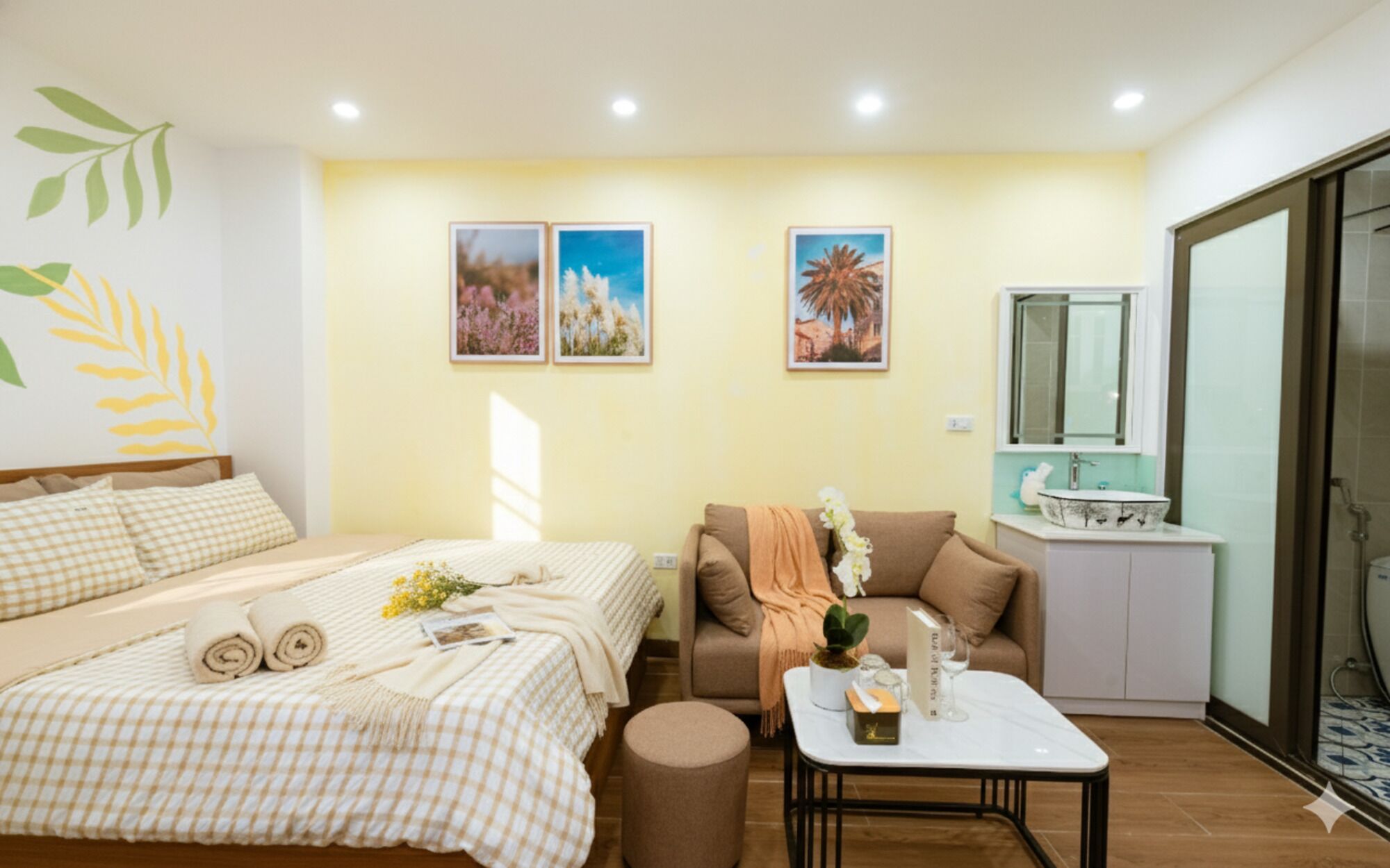A hotel room with a bed, a sofa, a small table, and a bathroom with a sink and mirror.