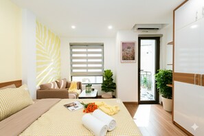 A hotel room with a bed, a sofa, a small table with a plant, a window with blinds, and a door leading to a balcony. - Aurelia Aparthotel Hanoi (Hanoi)