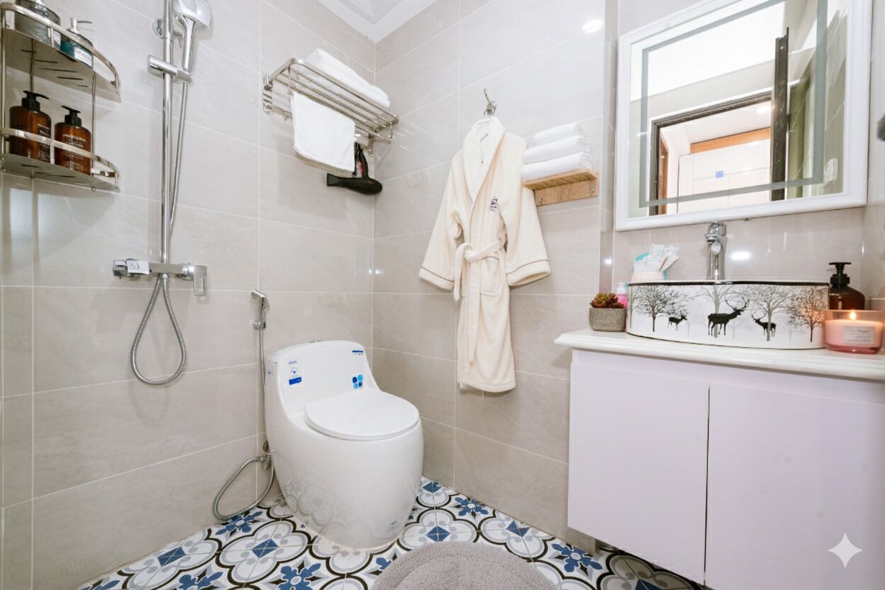 A bathroom with a toilet, shower, and sink. There are toiletries on a shelf, a towel rack, and a mirror above the sink.