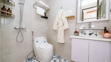 A bathroom with a toilet, shower, and sink. There are toiletries on a shelf, a towel rack, and a mirror above the sink.