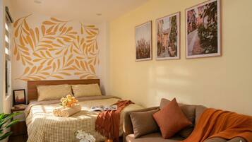 A hotel room with a large bed, a sofa, and a wall with leaf patterns and framed pictures.