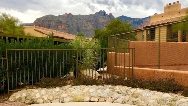 A swimming pool with a stone border, surrounded by a fence and a stone wall, with a mountainous backdrop. - Foothills 2-bedroom condo in welcoming Tucson with AC and fitness room (Tucson)